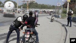 হাইতির পোর্ট-অ-প্রিন্স-এর একটি তল্লাশি চৌকিতে এক মোটরসাইকেল আরোহীর দেহ তল্লাশি করছেন এক পুলিশ; ১ জুলাই ২০২৩। 