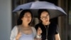 People use an umbrella to shield themselves from the sun as they walk along a street on an unseasonably hot day in Beijing, June 24, 2023. 