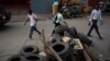 FILE - People pass a barricade that closes the entrance for vehicles after 6 p.m. erected by the Bwa Kale movement, an initiative to fight gangs seeking to take control of the neighborhood, in the Canape Vert area of Port-au-Prince, Haiti, May 31, 2023.