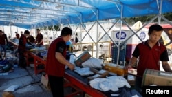 FILE - Delivery workers sort packages on a conveyor belt, ahead of the '618' shopping festival, at a logistics station in Beijing, June 12, 2023. 