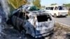 Sebuah minibus bergerak melewati mobil yang terbakar yang digunakan oleh komandan senior Hizbullah, Wissam Tawil, yang tewas dalam serangan Israel di desa Kherbet Selem, Lebanon selatan, pada 9 Januari 2024. (Foto: AP/Hussein Malla)