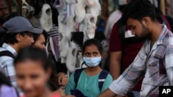 Seorang gadis mengenakan masker di antara kerumunan warga yang berlalu-lalang di distrik perbelanjaan Mumbai, India, Kamis, 22 Desember 2022. (AP /Rafiq Maqbool)