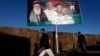 Men walk past a campaign banner of Afghan presidential candidate Abdul Rassoul Sayyaf, in Kabul, Feb. 9, 2014.