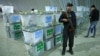 An Afghan police officer stands guard as election workers (R) note serial numbers of ballot boxes at a warehouse of the Independent Elections Commission warehouse in Kabul, April 6, 2014.