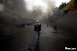 An opposition supporter walks amid smoke during clashes with police after the Organization of American States rejected a declaration of victory for Honduran President Juan Orlando Hernandez in a sharply disputed election, in Tegucigalpa, Dec. 18, 2017.