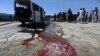 Afghan residents watch as a man washes a damaged minivan after it was hit by a remote-controlled bomb in Kabul, July 15, 2014. 