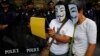 FILE - Anti-government protesters wearing Guy Fawkes masks use an iPad in front of riot policemen during a rally outside a shopping mall in Bangkok, June 9, 2013. 