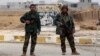 FILE - Kurdish Peshmerga fighters stand in a street against the backdrop of a defaced Islamic State flag in the town of Sinjar, northern Iraq, Nov. 16, 2015.