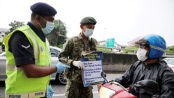 Un soldado y un oficial de policía con máscaras protectoras muestran una pancarta a un motociclista en un bloqueo de carretera establecido para hacer cumplir la orden de control de movimiento debido al brote de COVID-19, en Kuala Lumpur, Malasia, 23 de marzo de 2020.