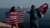 Yaney Cajigal, left, and Dalwin Valdes hold up U.S. and Cuban flags as they watch the arrival of Carnival's Adonia cruise ship from Miami, in Havana, Cuba, May 2, 2016.