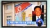 Passersby watch a local television broadcast in Seoul on May 2, 2013 showing a report and picture of Kenneth Bae (R), a Korean-American tour operator detained in North Korea, against the background of a North Korean flag painted on the wall of a building 