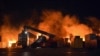Api muncul dari kontainer yang terbakar di lokasi serangan rudal, di pelabuhan kota pesisir Latakia, Suriah, Selasa, 28 Desember 2021. (Foto: SANA via AP)
